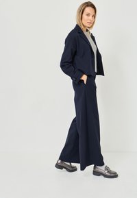 Navy pinstriped suit with a cropped jacket and wide-leg pants. Features a gray top and metallic shoes with a chunky sole. Smooth texture.