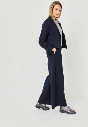 Marineblauwe gestreepte suit met een cropped jasje en wijde broekspijpen. Bevat een grijze top en metallic schoenen met een chunky zool. Glad textuur.