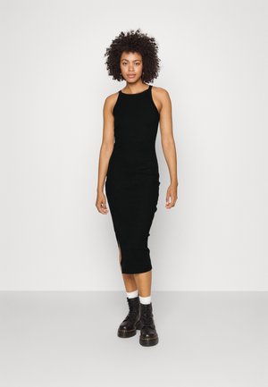 Vestido midi negro acanalado con un diseño ajustado, aberturas laterales y sin mangas. Lleva botas negras con cordones y calcetines blancos.