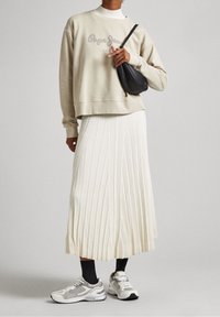 beige sweatshirt med "Pepe Jeans" logotyp, vit plisserad kjol och grå sneakers. Svart crossbody-väska ger kontrast. Släta och texturerade tyger.