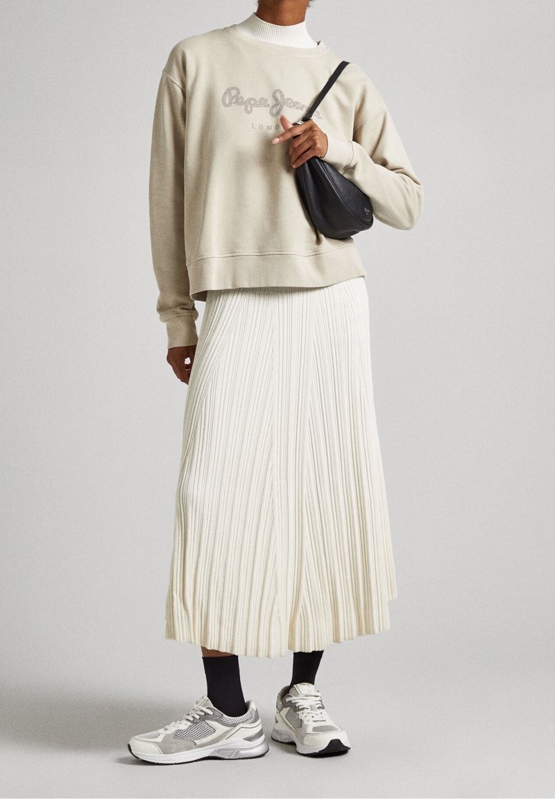 beige sweatshirt med "Pepe Jeans" logotyp, vit plisserad kjol och grå sneakers. Svart crossbody-väska ger kontrast. Släta och texturerade tyger.