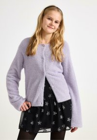 Lila donzige cardigan met knoopsluiting, lange mouwen en een zachte textuur, gecombineerd met een zwarte rok met zilveren sterrenpatronen.