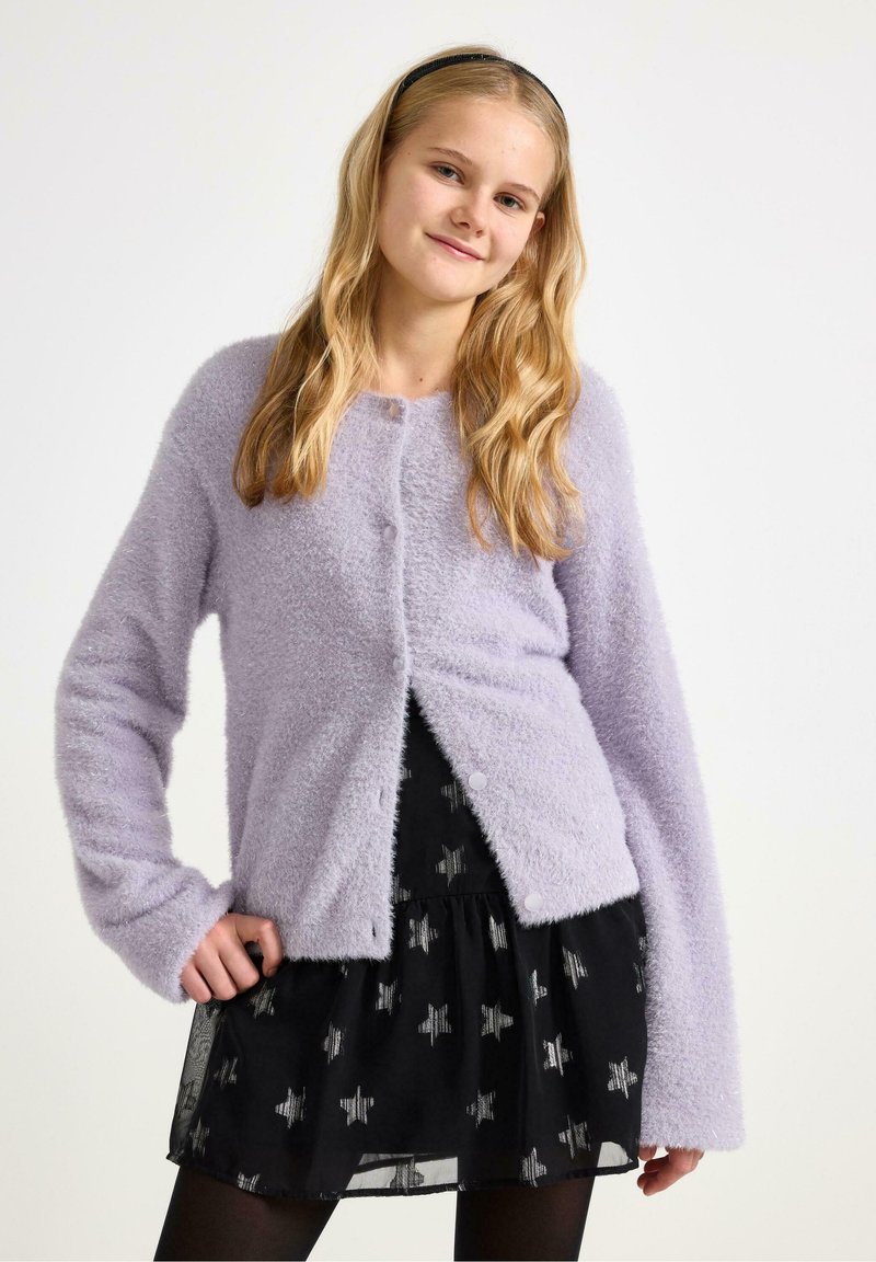 Lila donzige cardigan met knoopsluiting, lange mouwen en een zachte textuur, gecombineerd met een zwarte rok met zilveren sterrenpatronen.