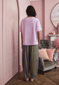 Light pink cotton t-shirt paired with loose, striped pajama pants in gray, yellow, and green. Background features soft pastel decor.