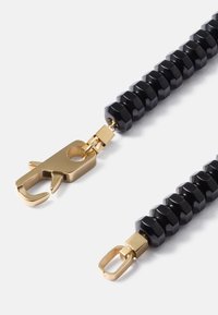 Bracelete composto por contas hexagonais pretas com fechos de metal dourado, apresentando uma textura suave e um acabamento brilhante. Os fechos possuem um design seguro e funcional.