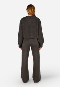 Šedý, huňatý svetr s kulatým výstřihem a spadlými rameny, doplněný šedými kalhotami s vysokým pasem a širokými nohavicemi. Měkká pletená textura po celém povrchu.