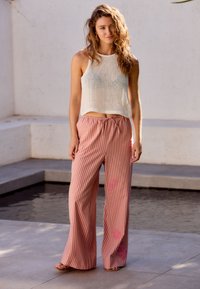 Un crop top blanc en tricot et un pantalon large rayé rose avec taille à cordon et accents floraux. Texture lisse et silhouette décontractée.
