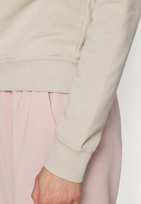 Tessuto di felpa beige con polsini a costina, abbinato a pantaloni rosa chiaro. Il tessuto sembra morbido con una vestibilità comoda.