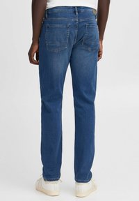 Jeans de mezclilla azul oscuro con un corte recto, presentan dos bolsillos traseros con costura en zigzag, y se llevan con zapatillas blancas.