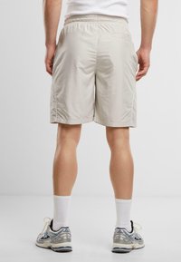 Hellbeige Sportshorts mit elastischem Bund, seitlichen Nähten, kontrastierendem weißen Besatz und einer Tasche. Getragen mit Laufschuhen und Socken.