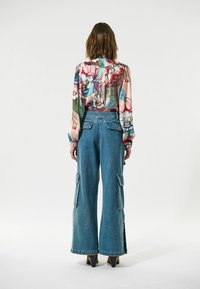 Blusa de estampado floral con mangas largas, combinada con pantalones cargo de mezclilla azul claro de pierna ancha y cintura alta, que cuentan con bolsillos laterales.