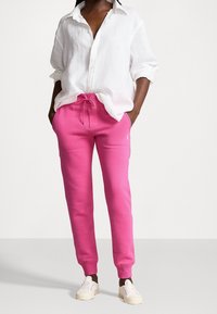 Rosa bomullsträningsbyxor med elastisk midja och dragsko, med sidofickor och muddar vid anklarna, ihop med en vit linneskjorta.