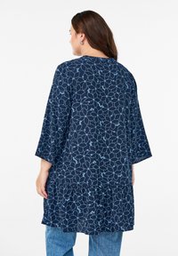 Navy tunic with light blue floral pattern, 3/4 sleeves, and a ruffled hem. Made of soft fabric, featuring a loose, relaxed fit.