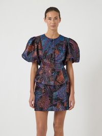 Donna che indossa un giubbotto aderente multicolore con maniche a sbuffo e una mini gonna abbinata, davanti a uno sfondo neutro.