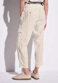 Hellbeige Leinen-Cargohosen mit elastischem Bund, Seitentaschen und lockerem Schnitt, kombiniert mit beigen strukturierten Schuhen.