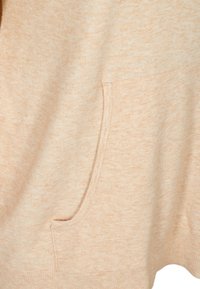 Tissu doux beige avec un motif tricoté texturé montrant un gros plan d'une poche kangourou avant sur un vêtement.