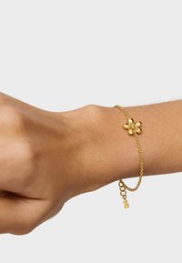 Pulsera de cadena de oro con un diseño floral de pétalos redondeados, asegurada con un pequeño cierre ajustable y una extensión de cadena.