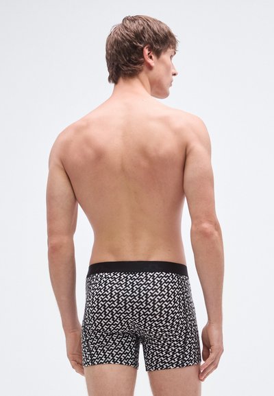 Boxers com padrão a preto e branco e cintura elástica, vistos por trás. Tecido liso com desenho geométrico.
