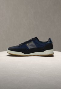 Baskets pour hommes bleu marine et noir avec semelle blanche, panneau latéral texturé, et logo "PS Paul Smith" en doré sur le côté.