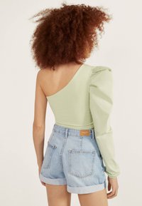 Vihreä yhden olkapään toppi puffihihalla, yhdistettynä korkeavyötäröisiin vaaleansinisiin farkkusalaisiin, joissa on käännetyt helmat.