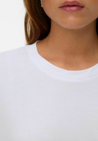 Vit bomull t-shirt med rund halsringning, slät textur och lätt ribbning vid kragen. Inga synliga mönster eller hårdvarudetaljer.