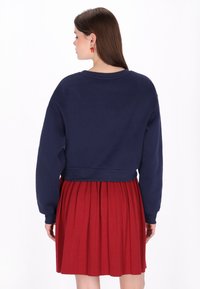 Tengerészkék hosszan érő pulóver hosszú ujjakkal, piros pliszírozott szoknyával párosítva. Simább anyag, kényelmes fazon és klasszikus kialakítás.