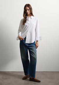 Camisa blanca de botones con un corte relajado, combinada con jeans de mezclilla azul holgados. Textura suave, colores contrastantes, diseño simple.
