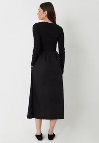 Vestido negro de manga larga con un corsé ajustado y falda acampanada. Fabricado en tejido suave, cuenta con bolsillos laterales y un diseño liso y minimalista.