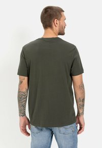 Oliven grøn T-shirt med korte ærmer og rund hals, lavet af bomuld. Har en afslappet pasform og synlige tatoveringer på armene.