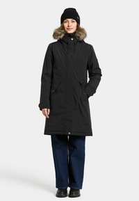 Zwarte parka met een met bont gevoerde capuchon, rits- en drukknoopsluiting, zijzakken en een middellange lengtedesign. Gekocht over donkere spijkerbroeken en laarzen.