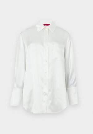 Blusa blanca de satén de manga larga con cuello puntiagudo, botones delanteros, bolsillo en el pecho y puños anchos sobre un fondo liso.