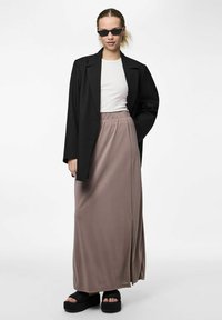 Svart blazer över en vit åtsittande topp och en lång taupekjol med en sidodel. Svarta plattformssandaler. Modellen bär smala svarta solglasögon.