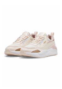Baskets Puma avec une tige rose pâle et crème, des panneaux texturés et une semelle blanche. Comprend une fermeture à lacets et des languettes pour tirer.