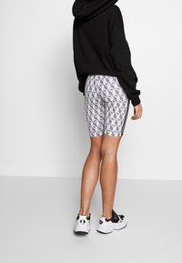 Svart huvtröja, mönstrade vita cykelbyxor med geometrisk design och svarta ränder på sidorna, bärs med svart-vita sneakers.