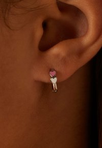 Herzförmige Ohrringe mit einem pinkfarbenen Emaille-Herz über einem weißen Emaille-Herz, beide aus silberfarbenem Metall gefertigt.