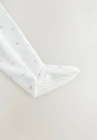 Fehér szövet papucs apró rózsaszín virágmintával, texturált gumitalppal a tapadásért, és lekerekített orr-résszel. Puha és rugalmas anyagból készült.