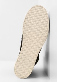 Semelle d'une basket avec une semelle extérieure en caoutchouc beige clair présentant un motif en forme de grille, sur un fond blanc uni.