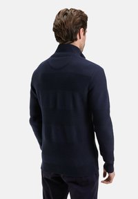 Pull en maille bleu marine à col montant, arborant un motif texturé de rayures horizontales et une base côtelée. Aucun matériel visible.