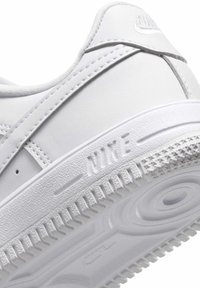 Biele tenisky so syntetickým zvrškom, textúrovanými detailmi a prešitými akcentmi. Obsahujú embosované logo Nike a gumovú podrážku s vzorovaným dezénom.