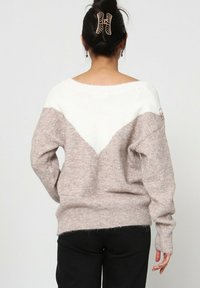 Pull en tricot rose clair et blanc avec un motif en chevron, col large et coupe ample. Les fentes sur les côtés et les poignets côtelés ajoutent de la texture.