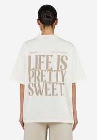 White oversized t-shirt made of cotton featuring beige text on the back that reads "LIFE IS PRETTY SWEET." Short sleeves and relaxed fit.