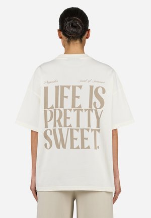 White oversized t-shirt made of cotton featuring beige text on the back that reads "LIFE IS PRETTY SWEET." Short sleeves and relaxed fit.