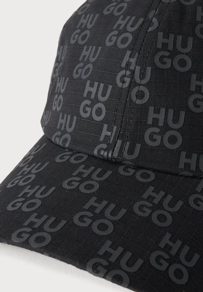 Casquette noire avec motif répétitif du texte "HUGO" gris foncé couvrant toute la surface, montrant les détails des panneaux cousus.