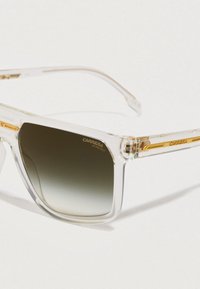 Óculos de sol com armação transparente, lentes escuras em degradê e detalhes em dourado, apresentando o logótipo Carrera e o rótulo de proteção UV.