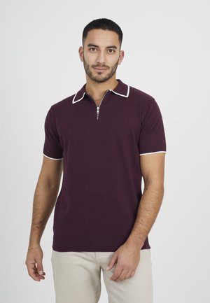 Polo a maniche corte bordeaux con colletto zip e dettagli bianchi, e polsini a costine. Realizzato in un tessuto liscio e leggero.