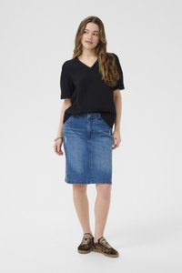 Haut noir texturé à col en v et manches courtes, associé à une jupe en jean bleu. Le modèle porte des baskets à imprimé léopard.