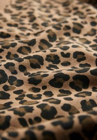 Luipaardprintstof toont onregelmatige zwarte vlekken op een tankleurige achtergrond, met een textuur die diepte aan het patroon toevoegt.
