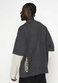 Przesadnie duża szara koszulka bawełniana o lekko teksturowanym wykończeniu. Posiada długie białe rękawy oraz nadruk "MULTIPLY APPAREL" w jasnym kolorze z boku.