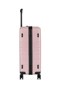 Harte pinke Reisetasche mit schwarzen Akzenten, vertikalen Rillen, Teleskopgriff und vier Rollen für Mobilität. Mit Reißverschluss.