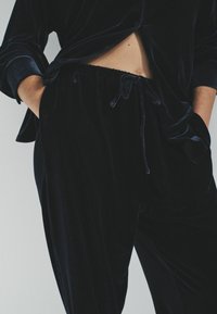 Samt-Loungewear-Set in tiefem Marineblau, bestehend aus einem lockeren Hemd mit Knöpfen und Hose mit elastischem Bund und Kordelzug, glatte Textur.